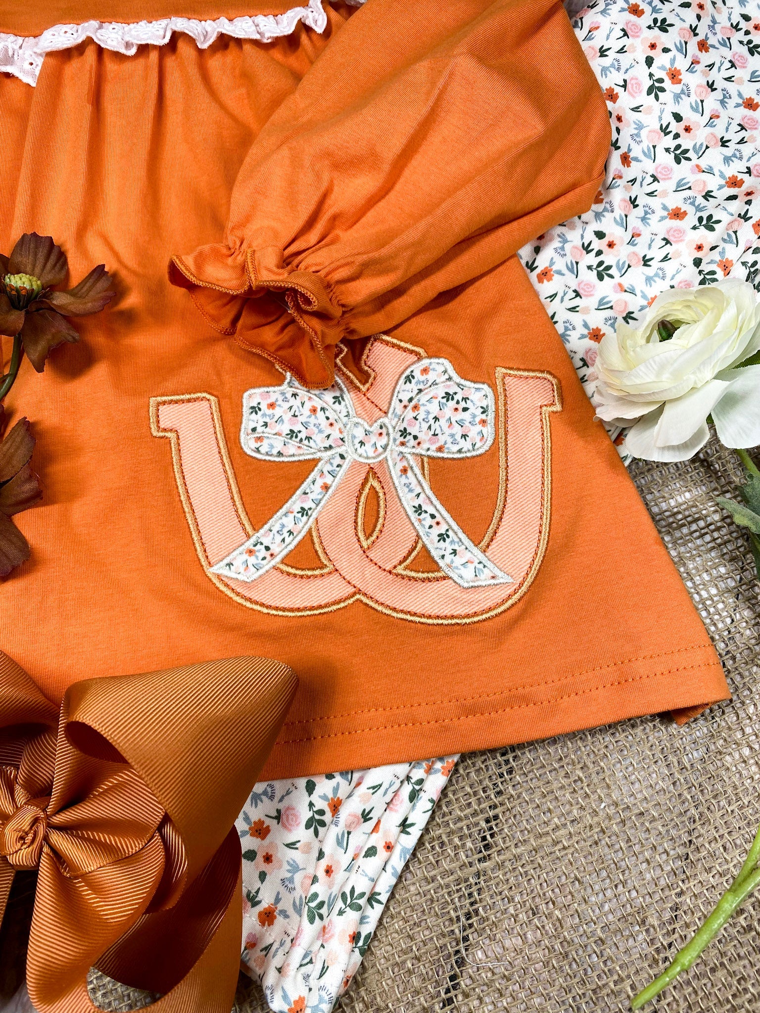 Girl wearing an orange horseshoe top with lace details and floral pants on a white background on a wooden background