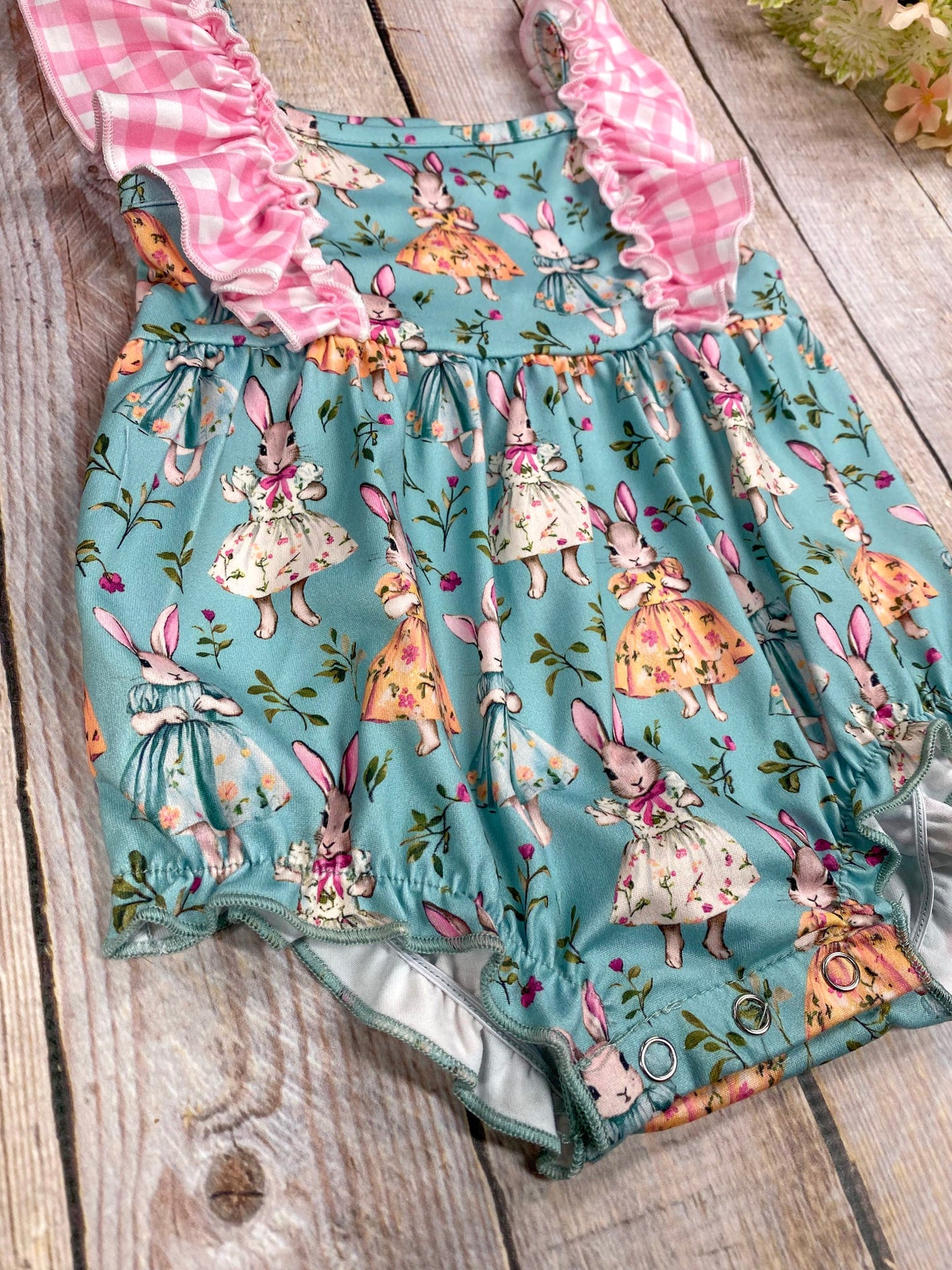 snap detail of romper with bunny print on a wooden surface