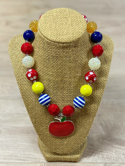 Red apple pendant chunky bead necklace with red polka dot, blue and white striped, white rhinestone, solid red, blue, and yellow beads, with a heart toggle closure.