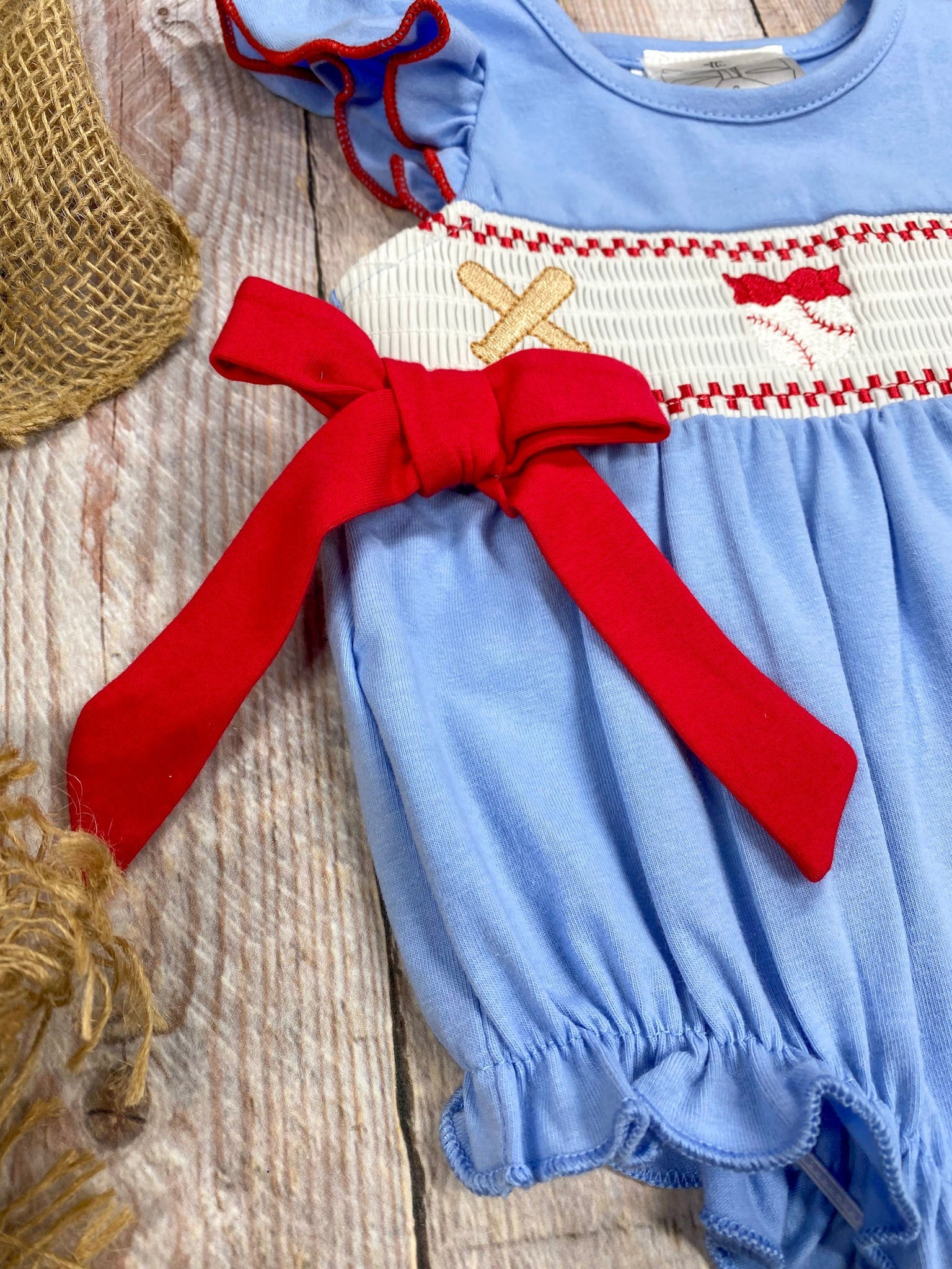 Baby romper with red bow and embroidered design on a wooden surface