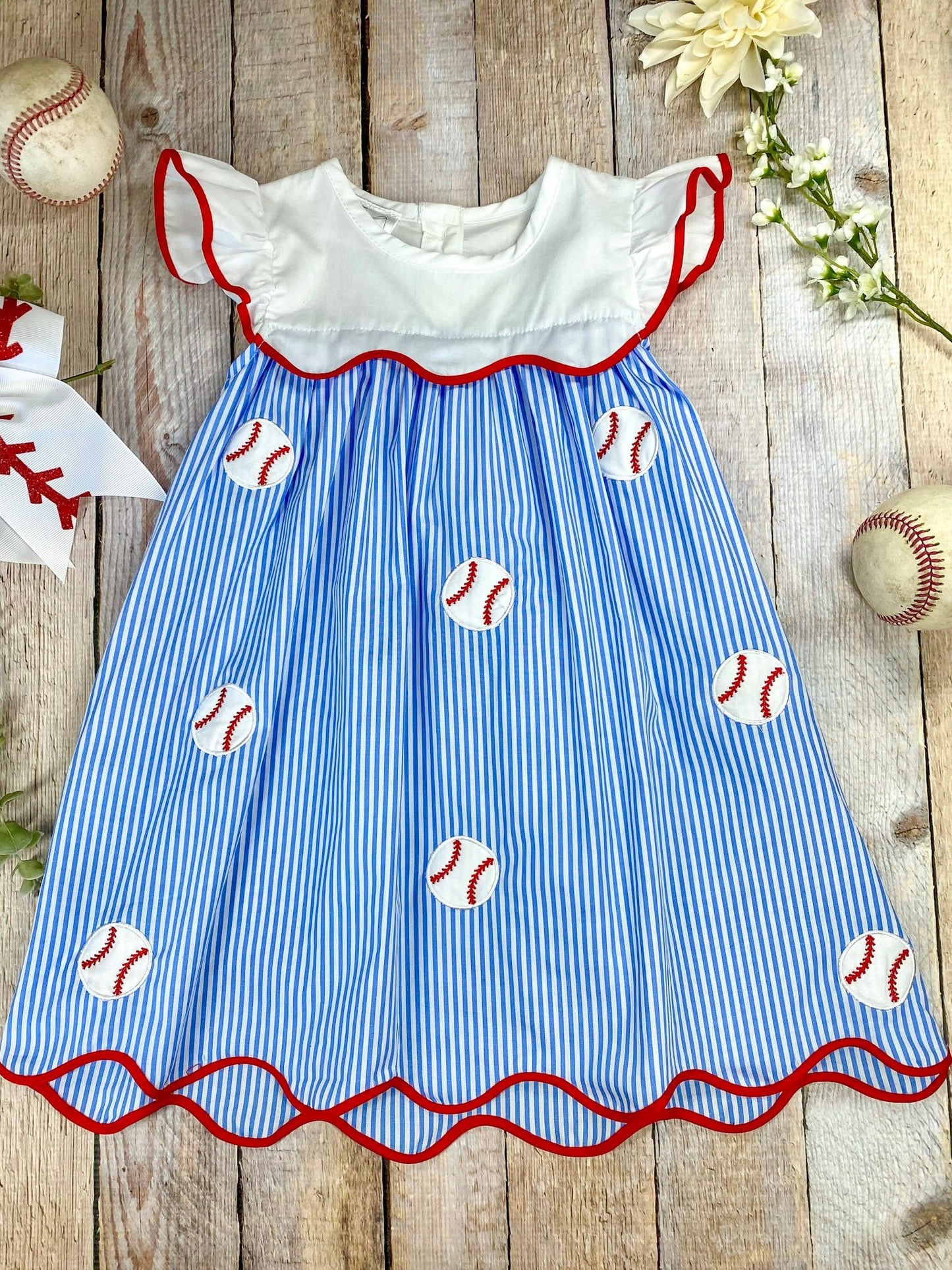 Girl's baseball dress with blue and white striped pattern and red trim on awooden background