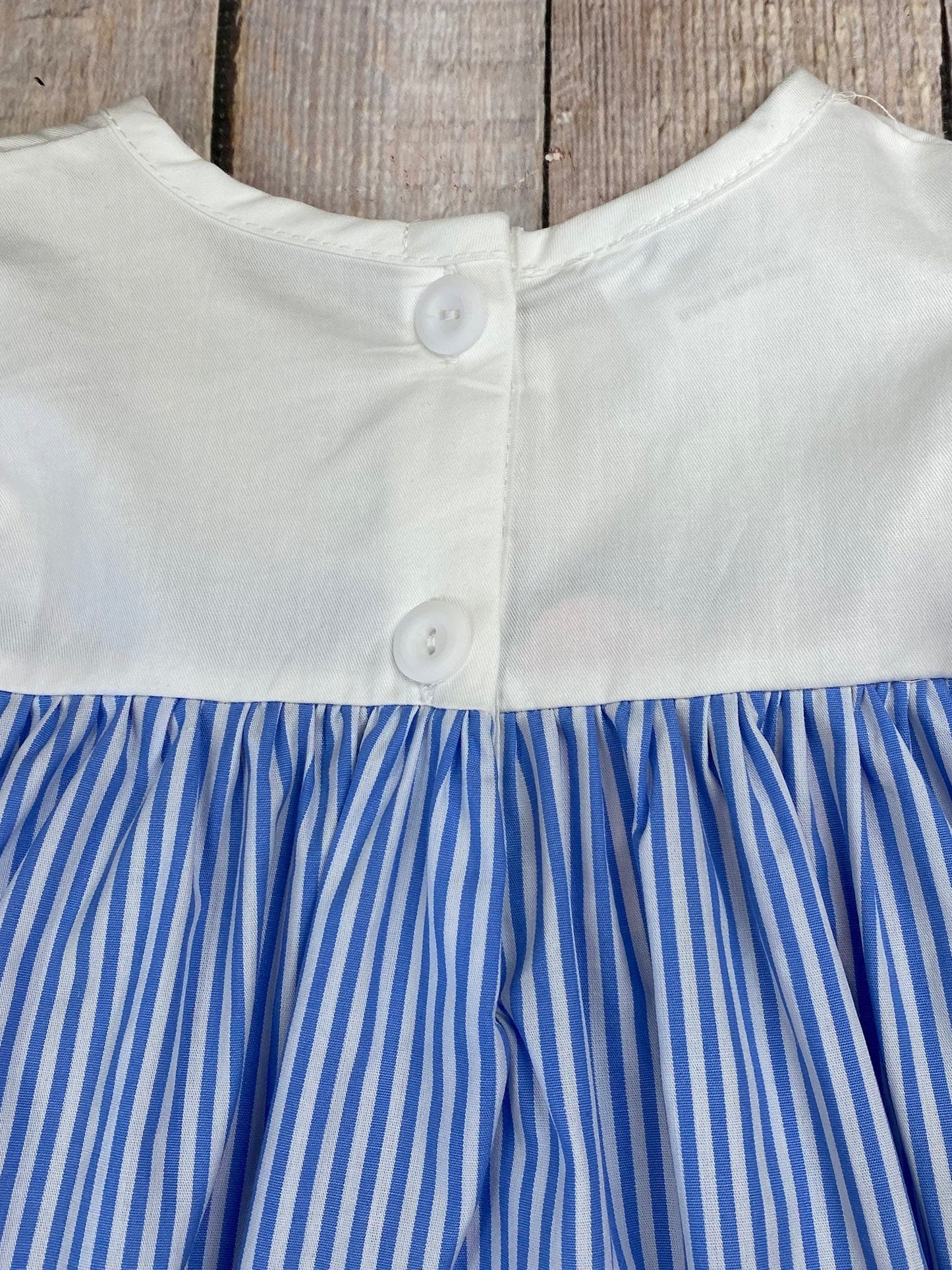 Close-up of a dress with white top and blue striped skirt against a wooden background