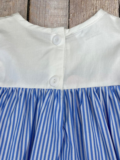 Close-up of a dress with white top and blue striped skirt against a wooden background