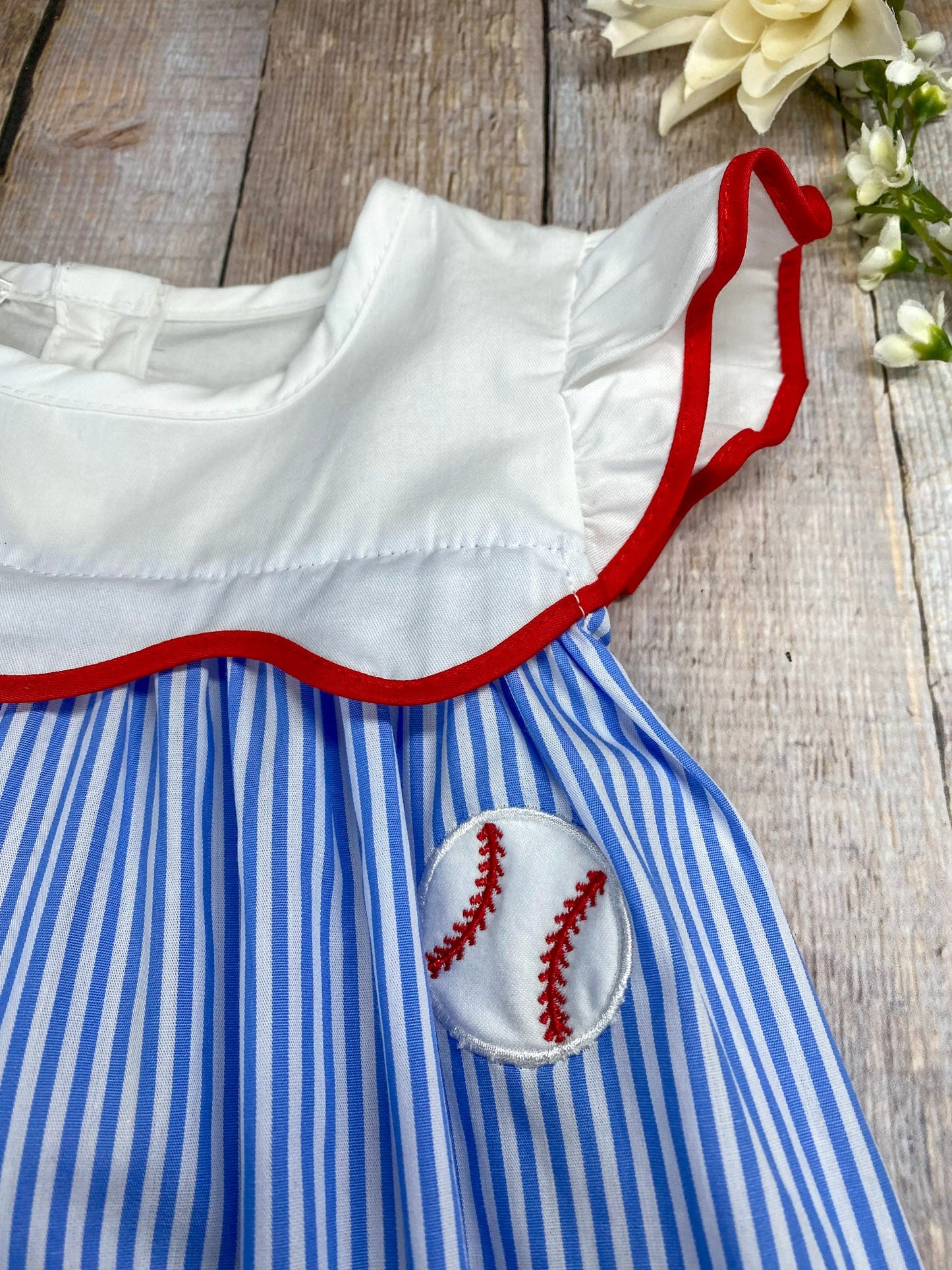 Girl's baseball dress with blue and white striped pattern and red trim on awooden background
