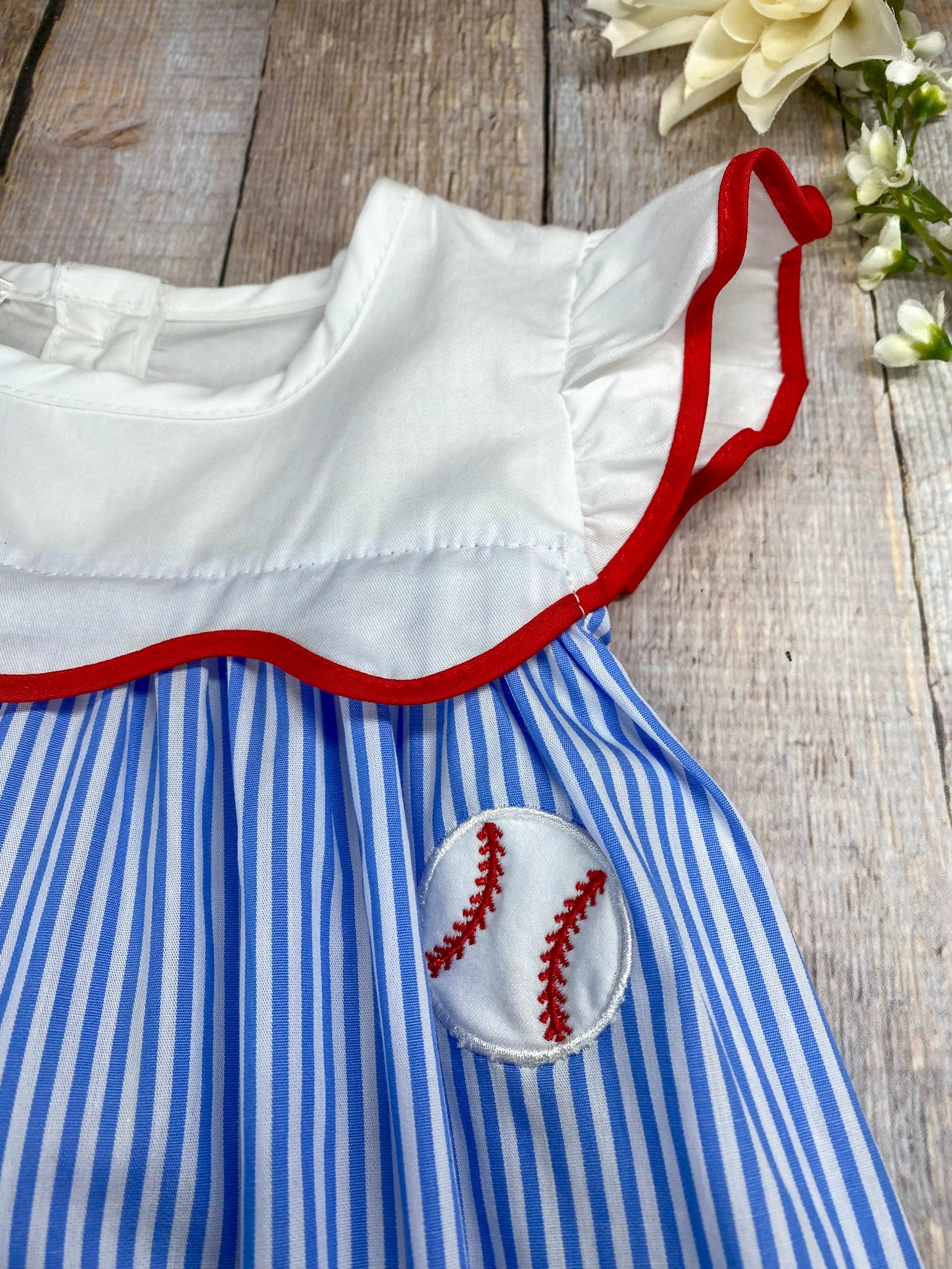 Girl's baseball dress with blue and white striped pattern and red trim on awooden background