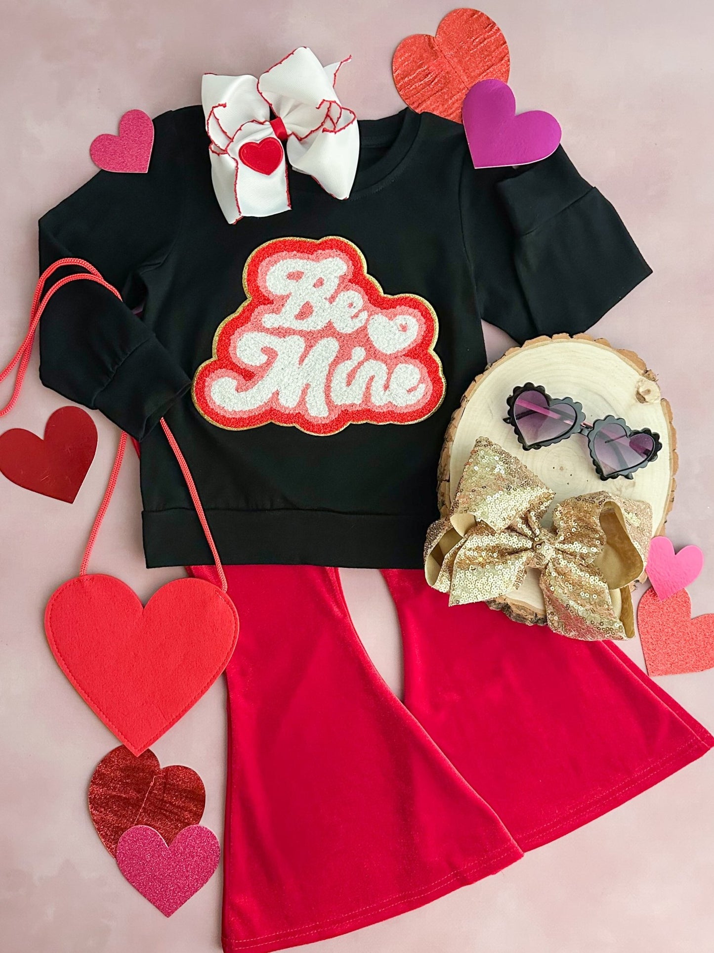 A red flared pants set with a black top that has 'BE MINE' written in heart graphics, accompanied by various heart-shaped accessories.