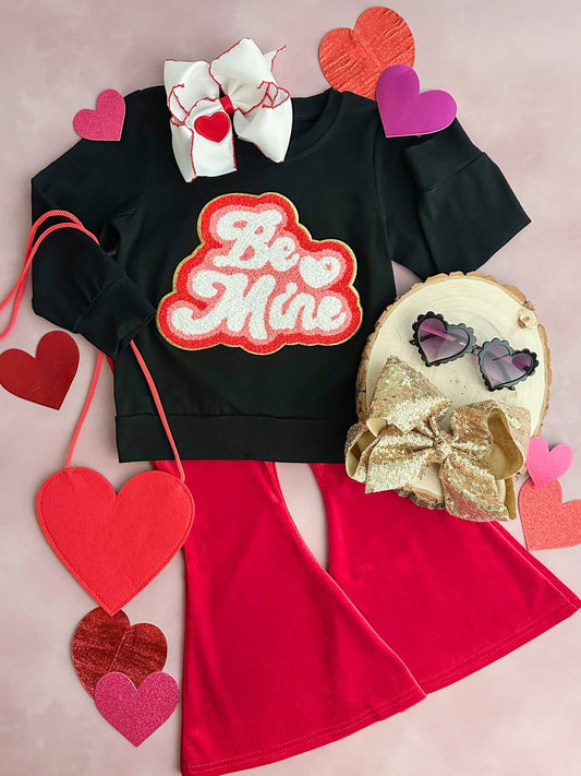 A red flared pants set with a black top that has 'BE MINE' written in heart graphics, accompanied by various heart-shaped accessories.