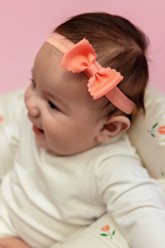 A baby wearing a pink scalloped bow headband.