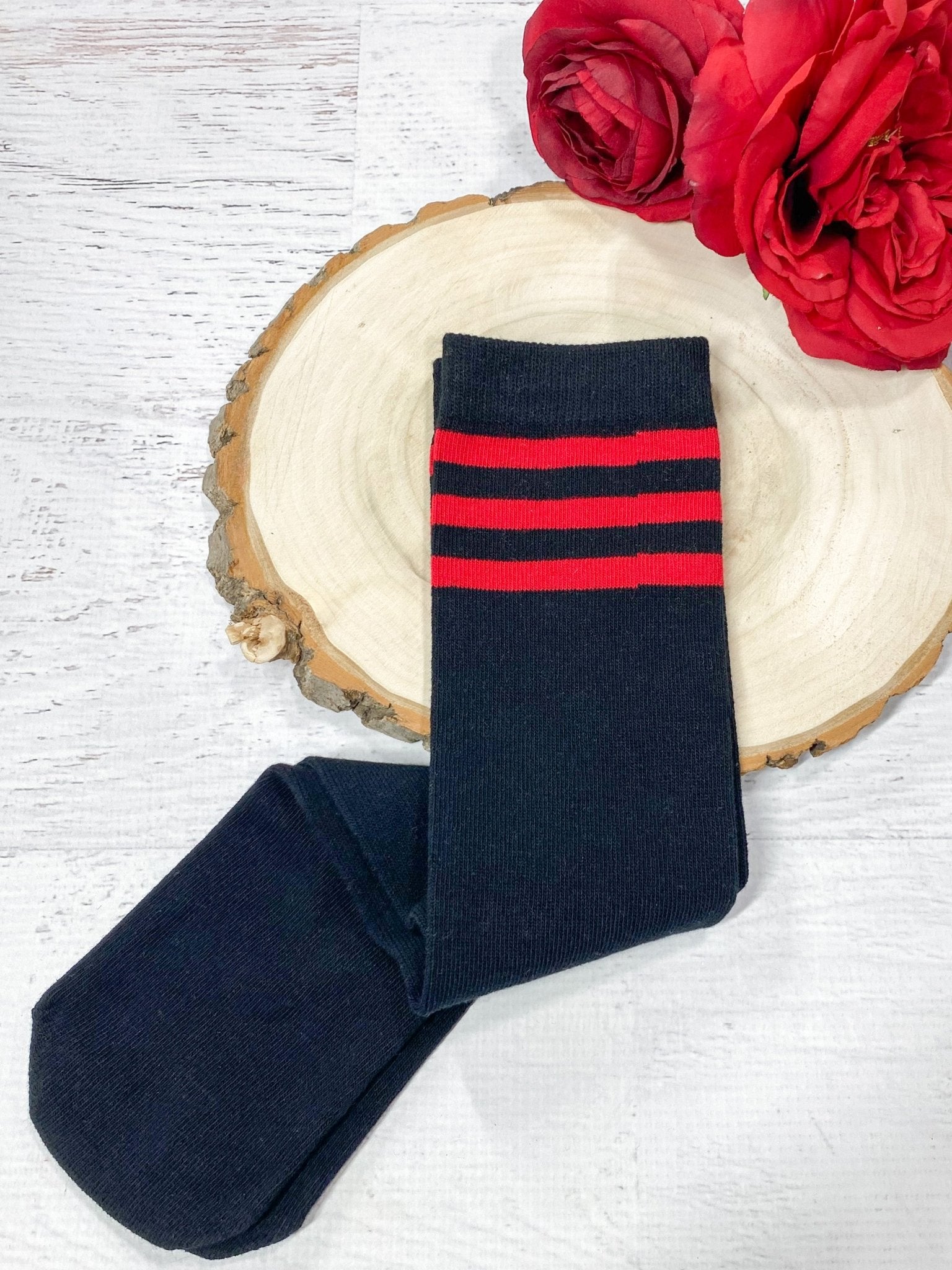 Pair of black socks with red stripes on a wooden surface with red flowers.