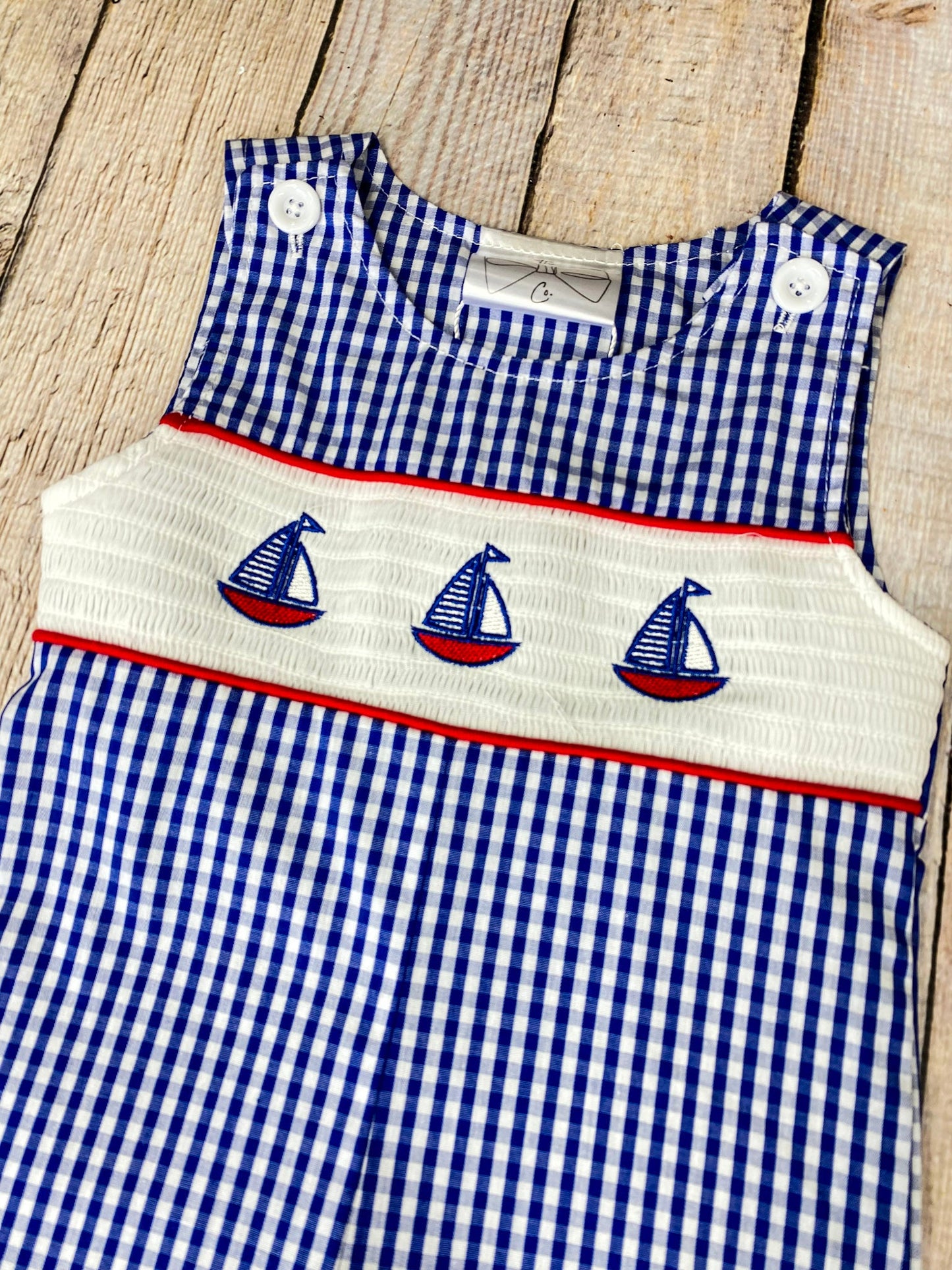 Blue checkered romper with sailboat design on a wooden background