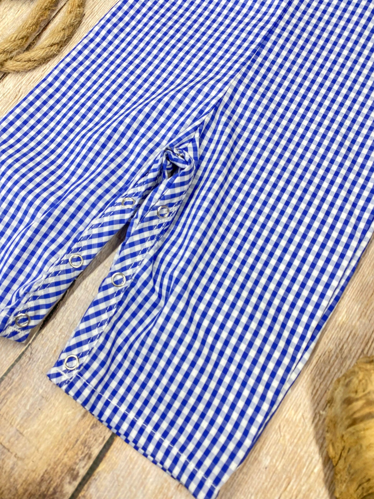 Blue checkered romper with sailboat design on a wooden background