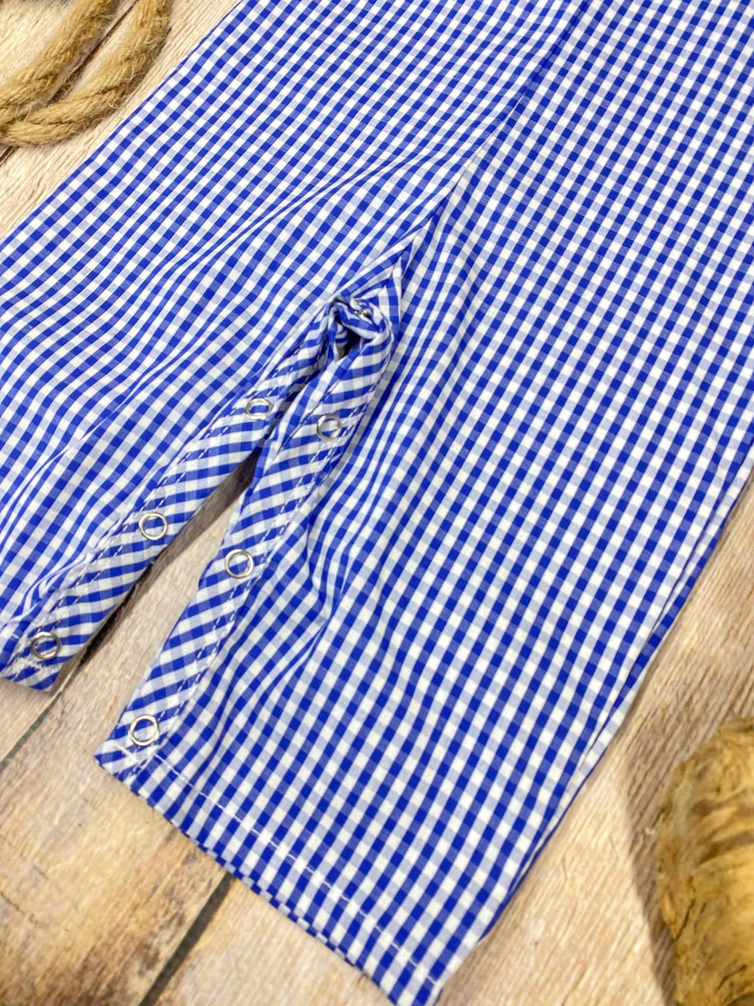 Blue checkered romper with sailboat design on a wooden background