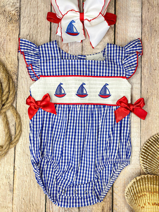 Blue checkered baby romper with sailboat design on a wooden background