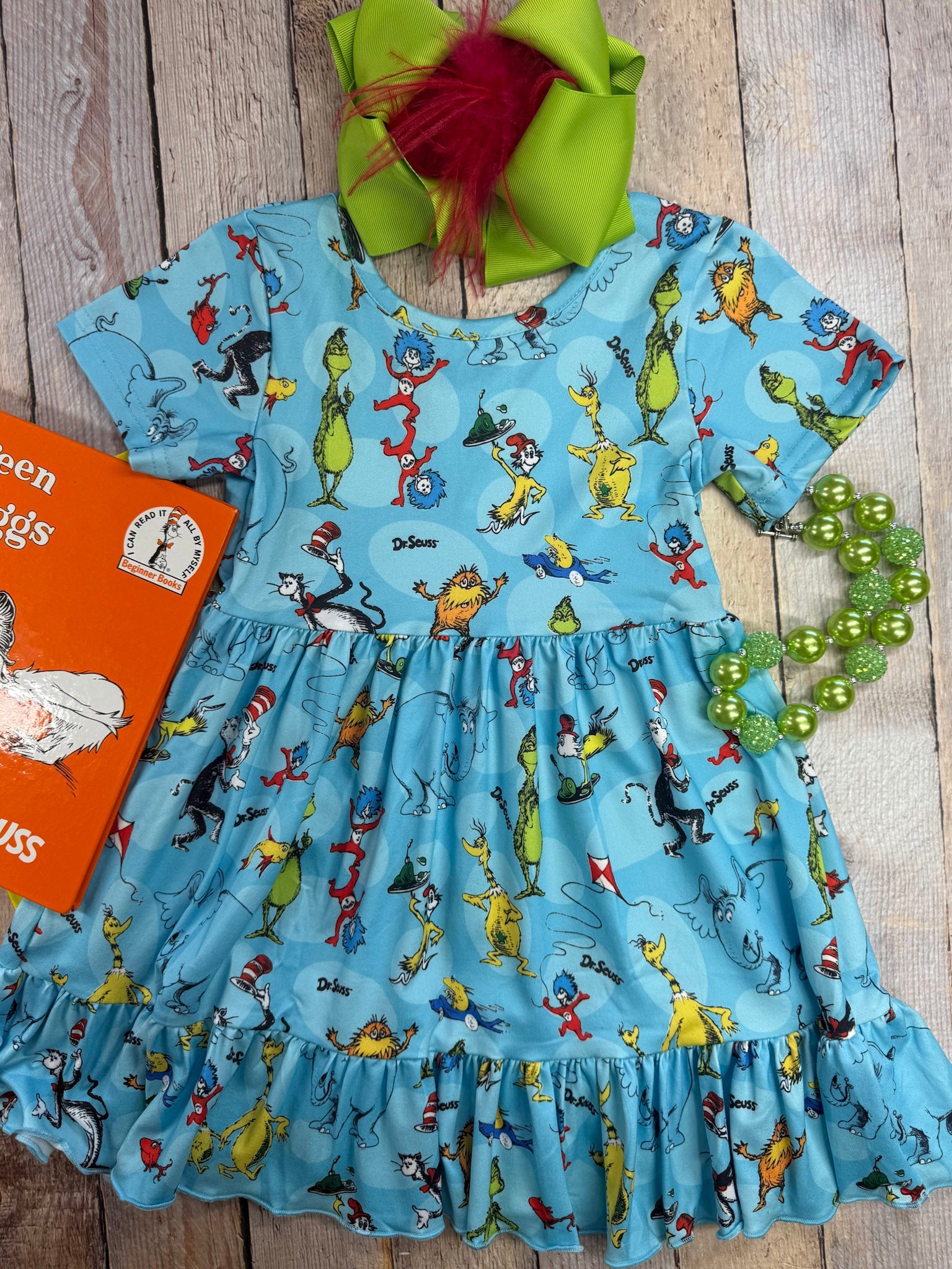 Children's dress with Dr. Seuss character print on a wooden surface, accompanied by a book and decorative items.