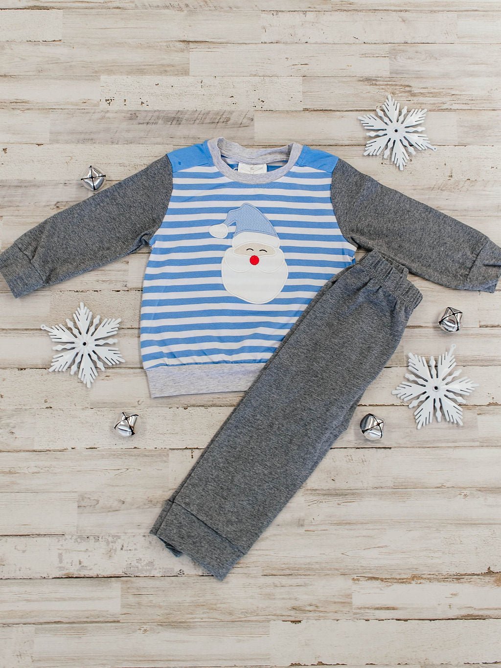 flat lay of an outfit featuring a blue and white striped long sleeve with a santa wearing blue hat applique and dark grey sleeves, paired with dark grey pants that match the sleeves