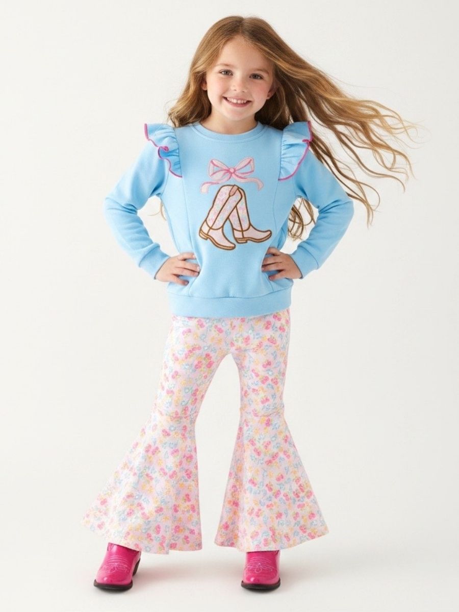 Girl wearing a blue top with boots, ruffles and floral pants on a white background