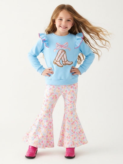 Girl wearing a blue top with boots, ruffles and floral pants on a white background