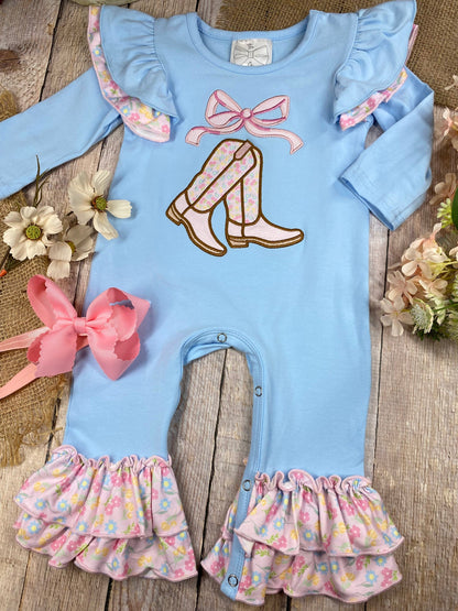 baby girl cowgirl one-piece with boots bow appliqué and floral ruffle leg hems on a wooden background