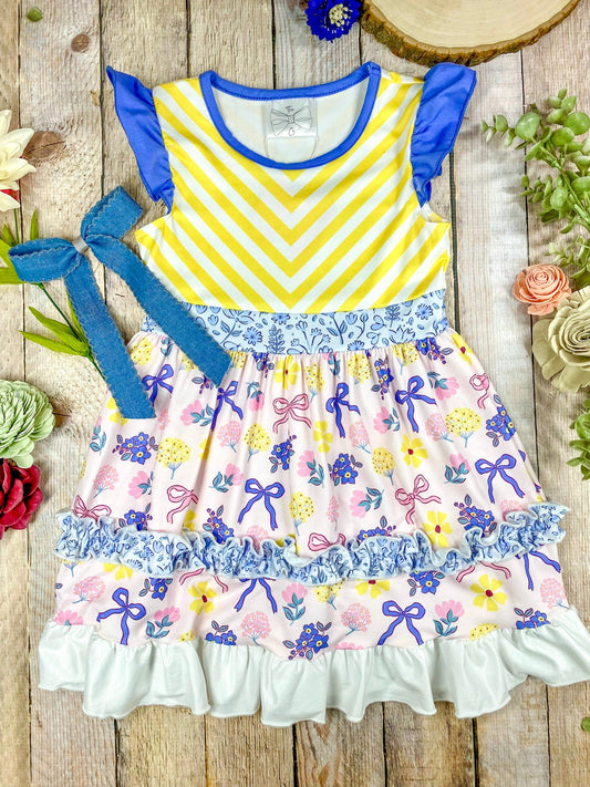 Colorful children's dress with yellow and purple striped top and floral skirt on a wooden background