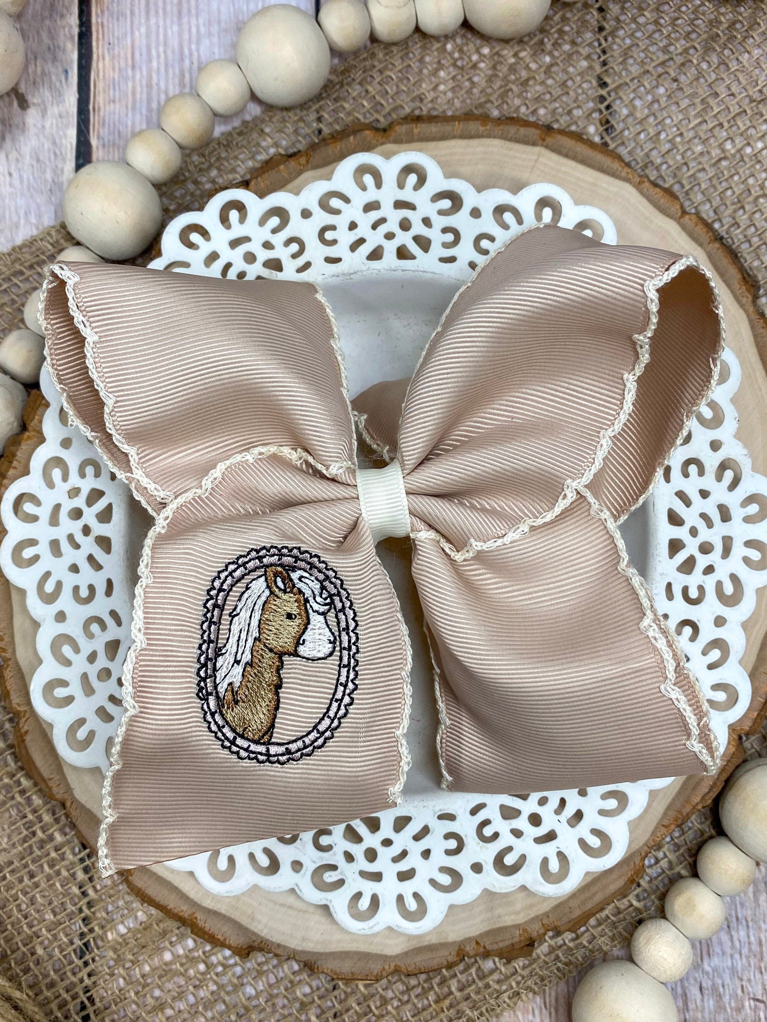 Large beige bow with a embroidered design on a decorative wooden board.