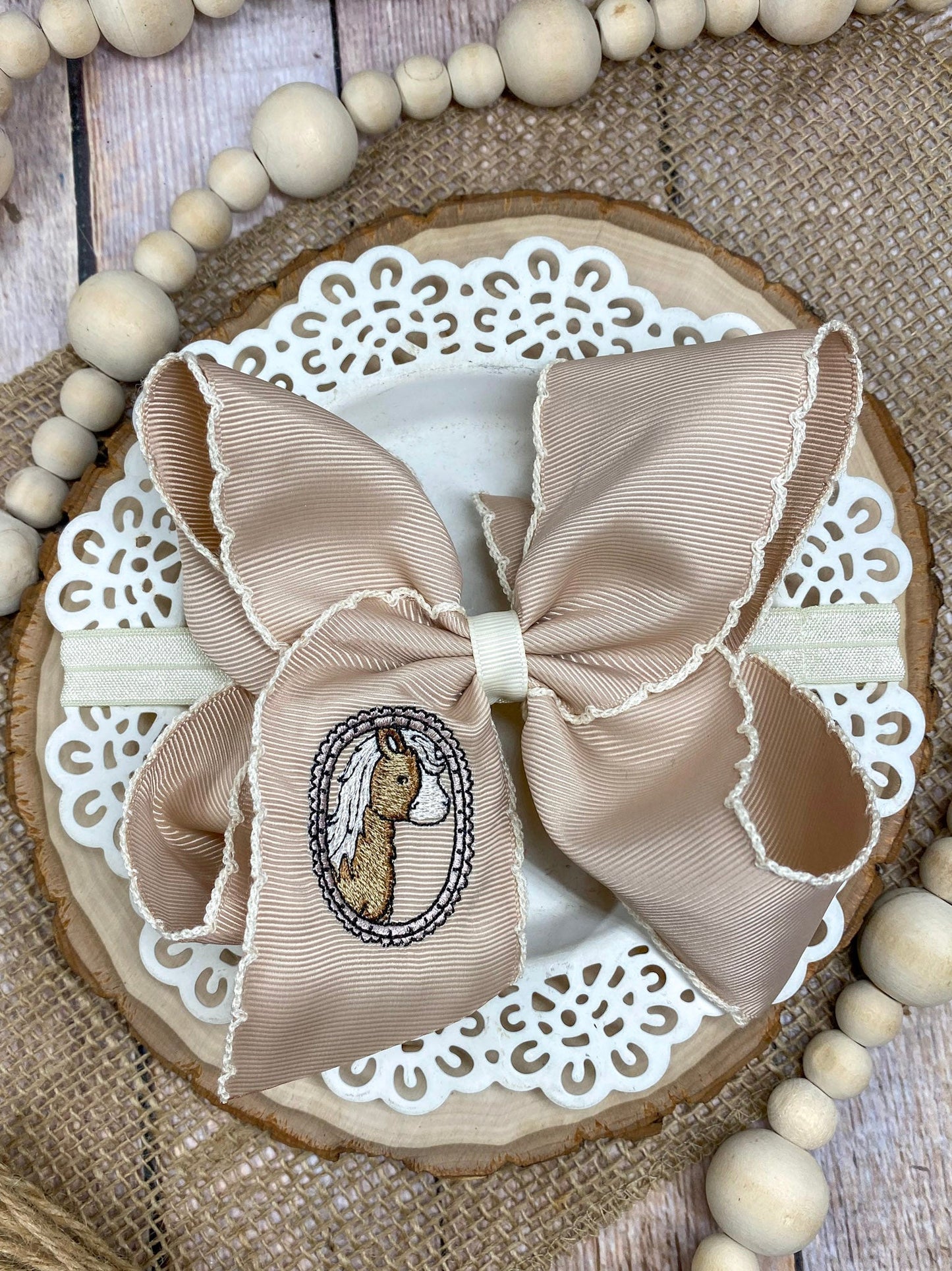 Beige bow with embroidered design on a decorative wooden board with beads.