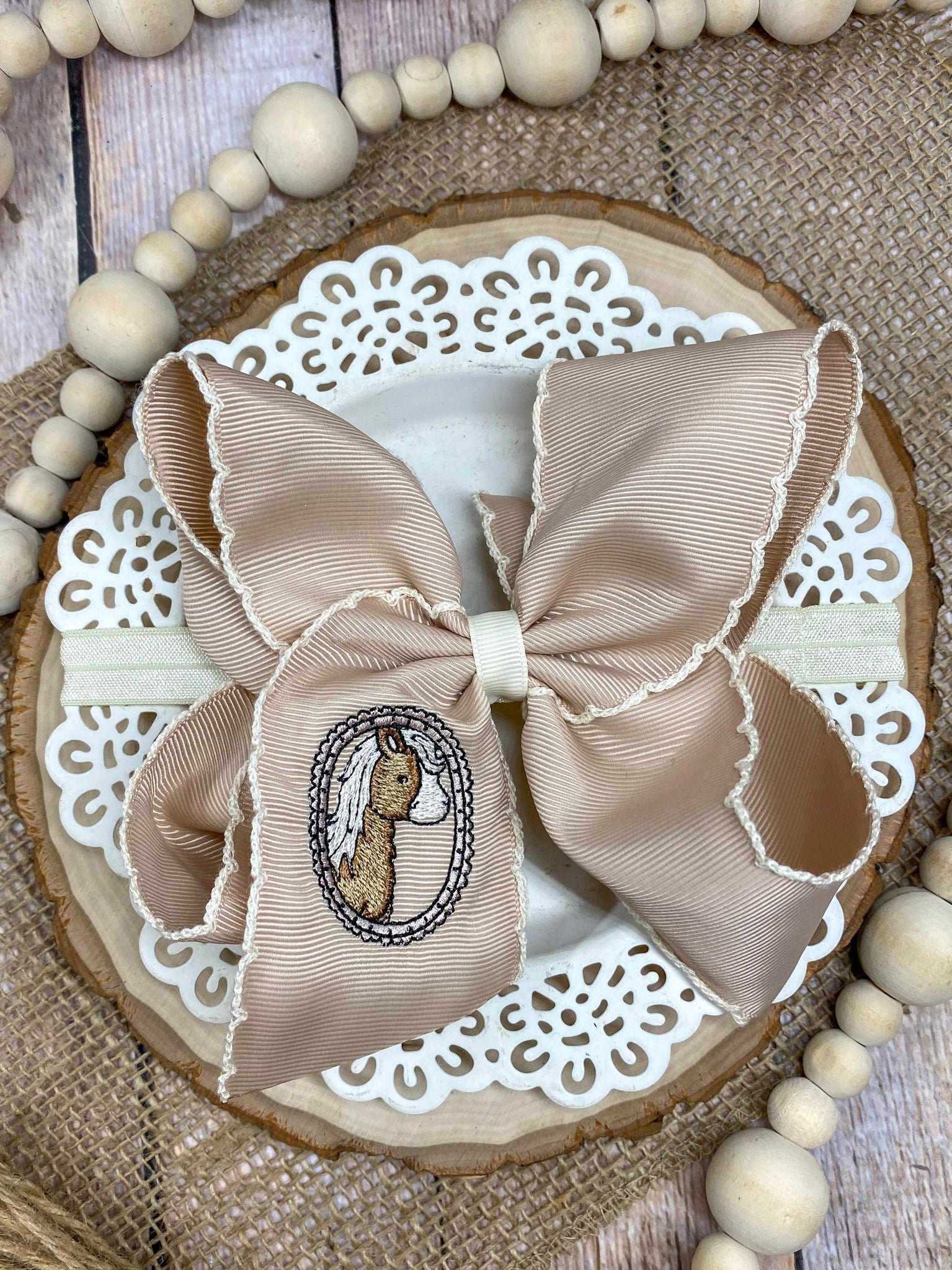 Beige bow with embroidered design on a decorative wooden board with beads.