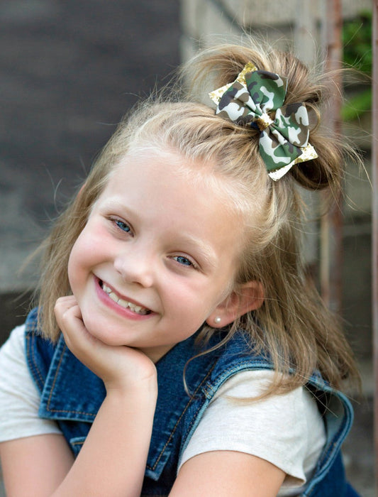 Girl wearing a camo and gold glitter hair bow