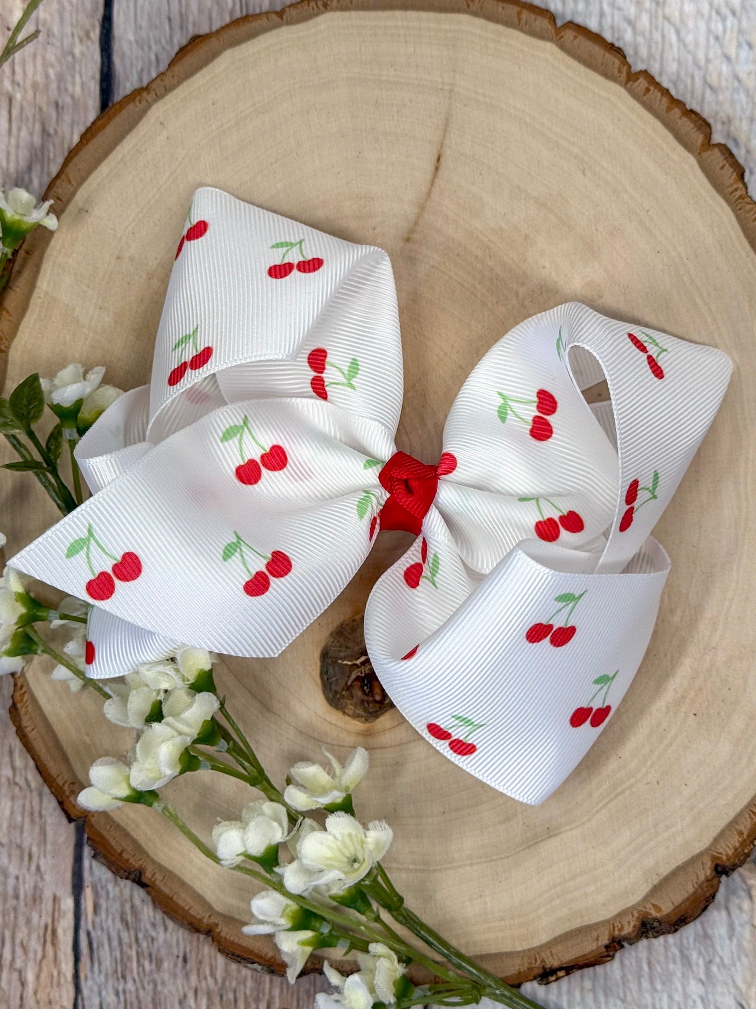 Cherry print grosgrain hair bow with red center knot on wooden background