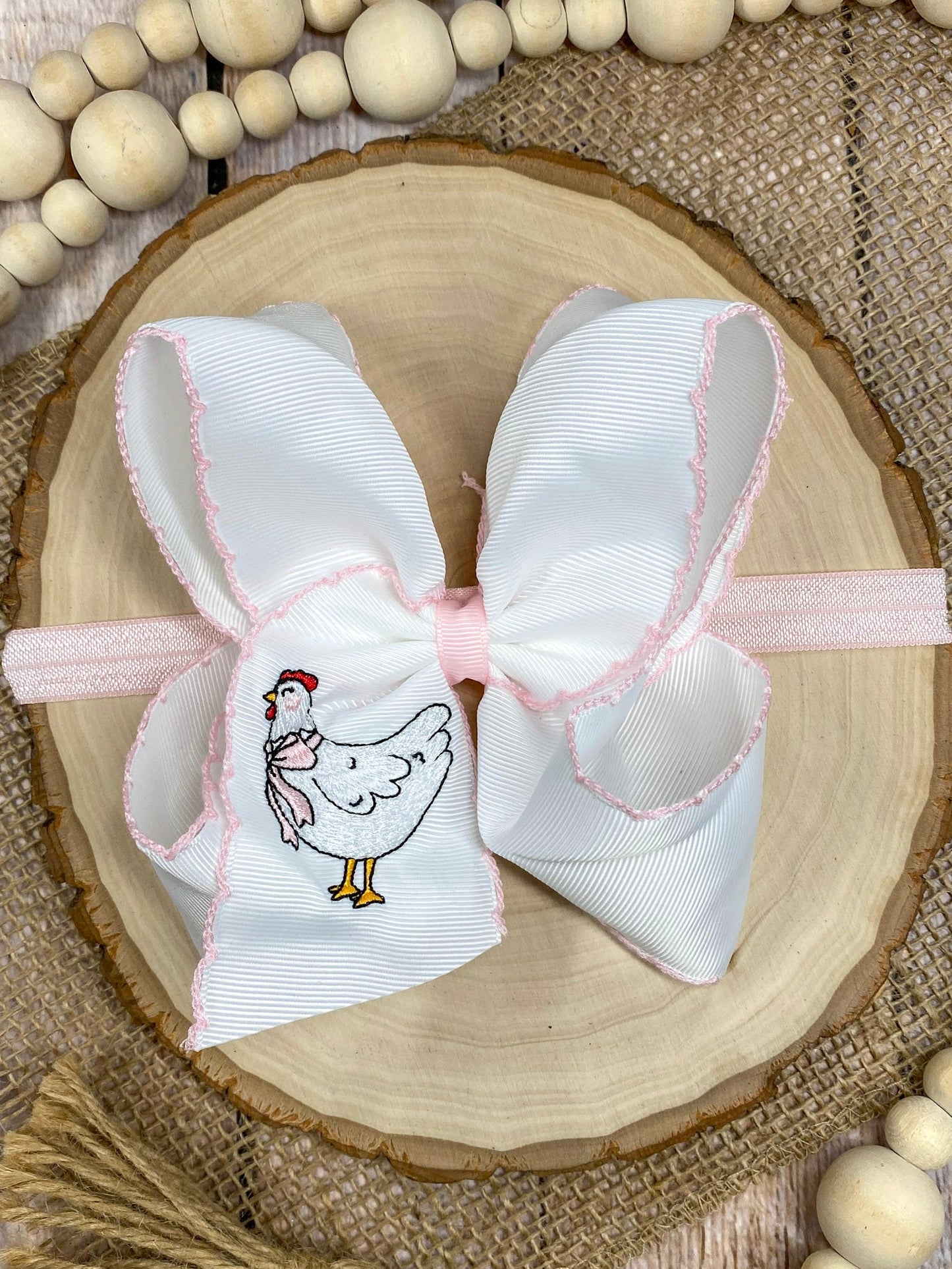 White hair bow with pink accents and a chicken illustration on a wooden surface.