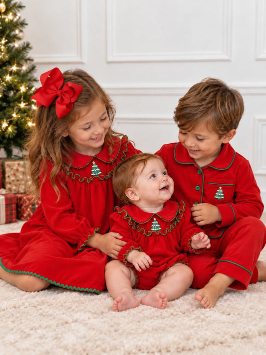 Three siblings wearing matching red Christmas pajamas with green trim and embroidered Christmas trees, posed together beside a decorated Christmas tree.