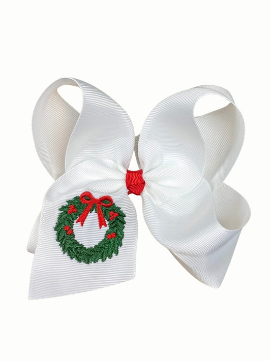 White grosgrain hair bow with an embroidered green Christmas wreath with red berries and bow on the tail, red center knot, on a white background