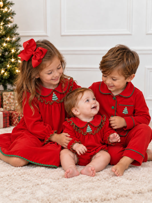 Three siblings wearing matching red Christmas pajamas with green trim and embroidered Christmas trees, posed together beside a decorated Christmas tree.