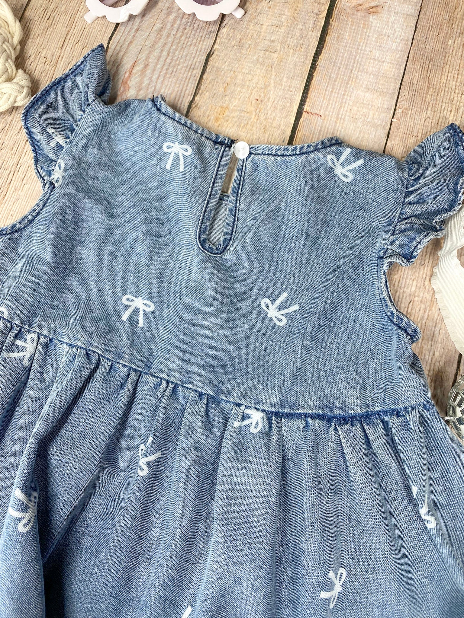 Blue denim bow print dress with ruffled sleeves and bottom on a wooden surface