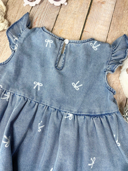 Blue denim bow print dress with ruffled sleeves and bottom on a wooden surface