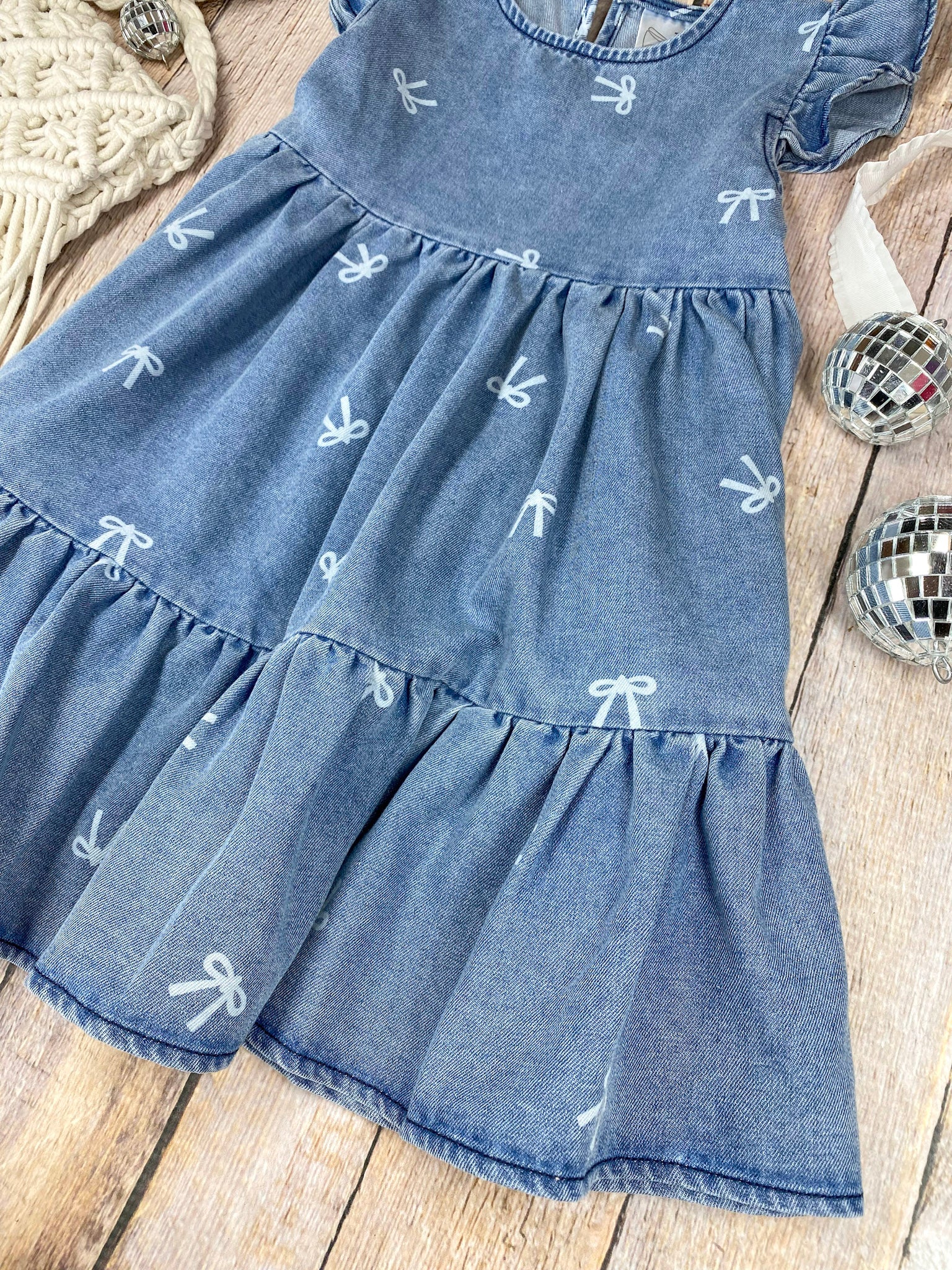 Blue denim bow print dress with ruffled sleeves and bottom on a wooden surface