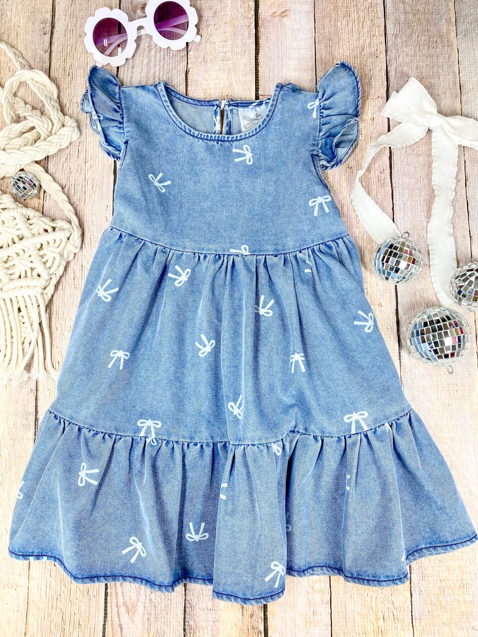 Blue denim bow print dress with ruffled sleeves and bottom on a wooden surface