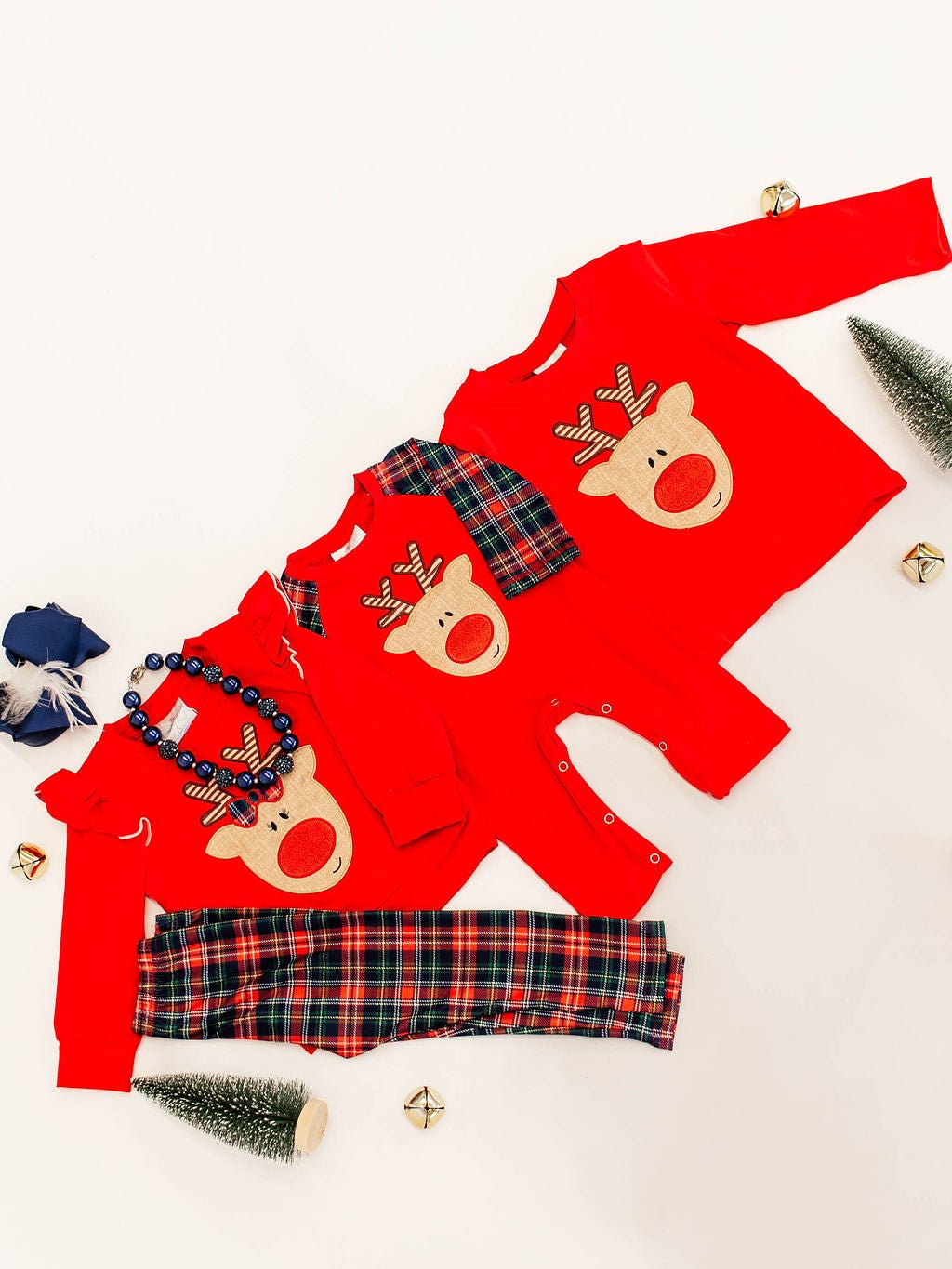 flat lay of a sibling set showing 3 outfits; far left is girls outfit with red long sleeve with a rudolf applique in the center paired with red and green plaid pants with a matching boy infant romper also red long sleeved with same rudolf applique in center and the red adnd green plaid sleeves and far right shows boys red long sleeve shirt with same rudolf applique