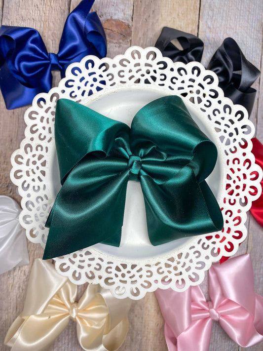 4.5 inch classic satin hair bow in hunter green on a white decorative plate surrounded by other satin bows in pink, ivory, white, navy, black, and red