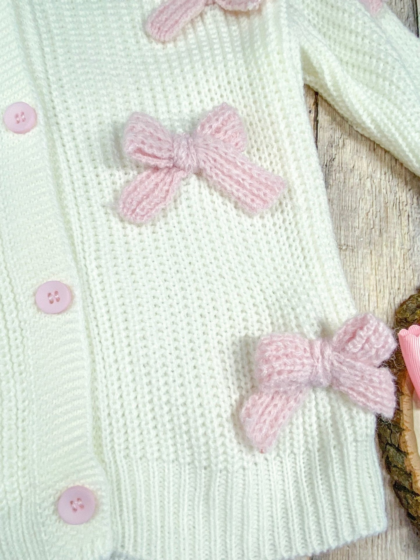 close up of the light pink knitted bows sewn onto sweater/cardigan