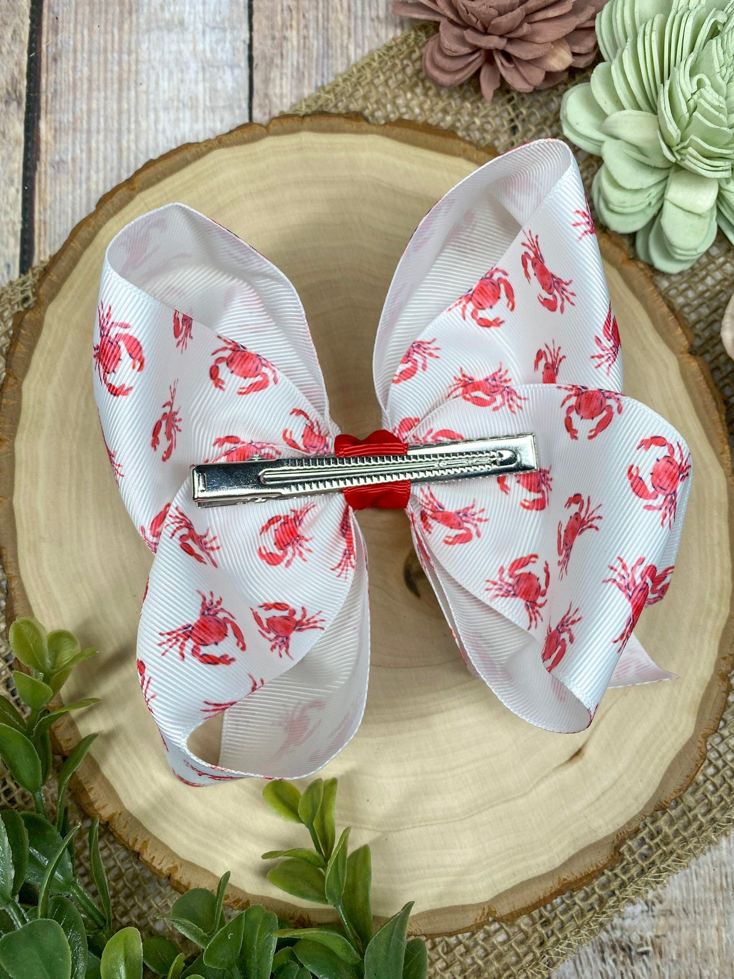 White hair bow with red patterns on a decorative plate with flowers in the background
