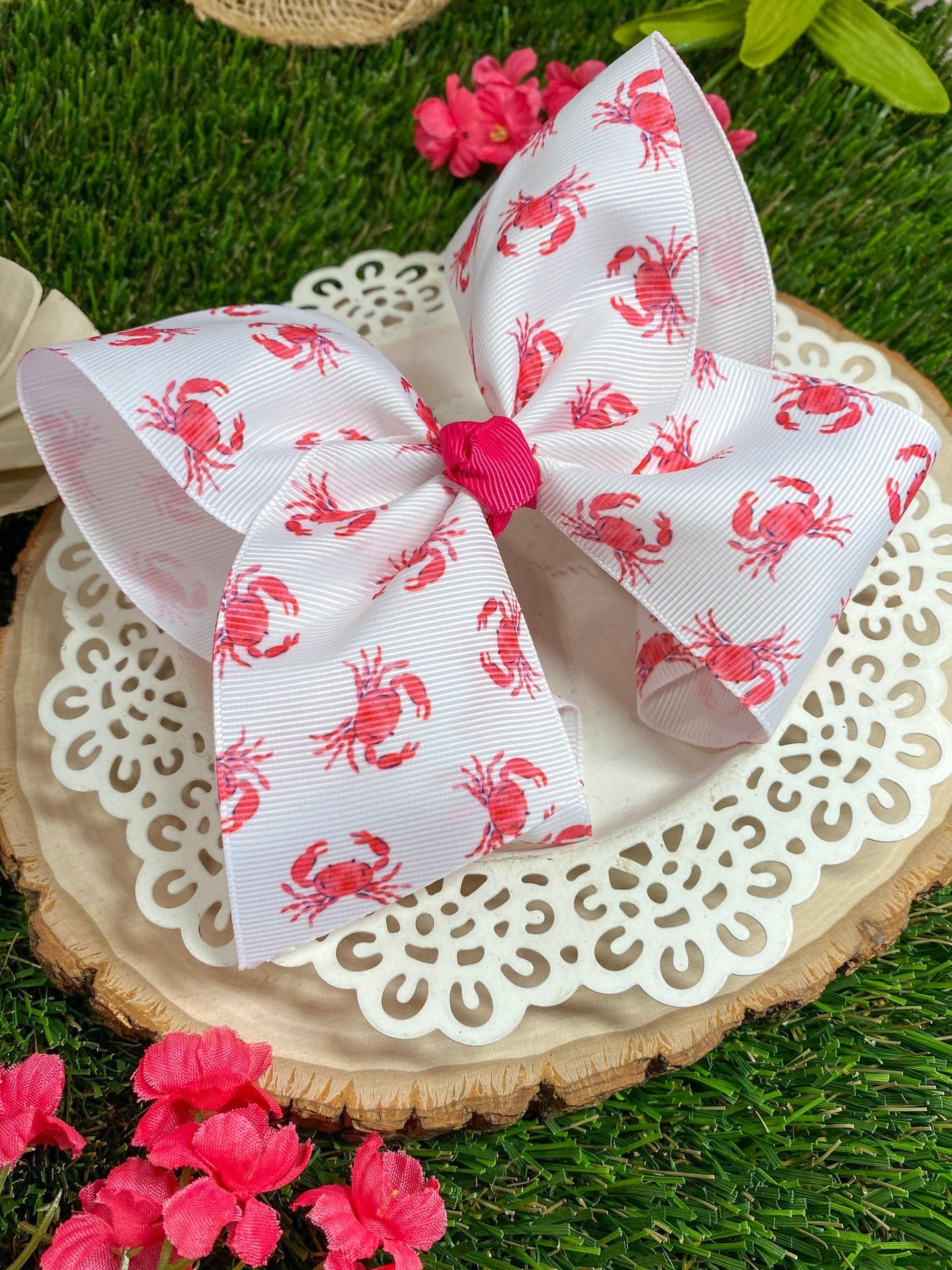 White bow with red crab pattern on a wooden slice with flowers in the background