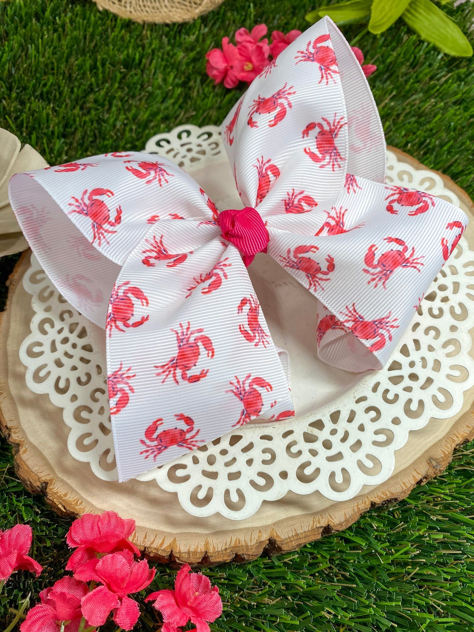 White bow with red crab pattern on a wooden slice with flowers in the background