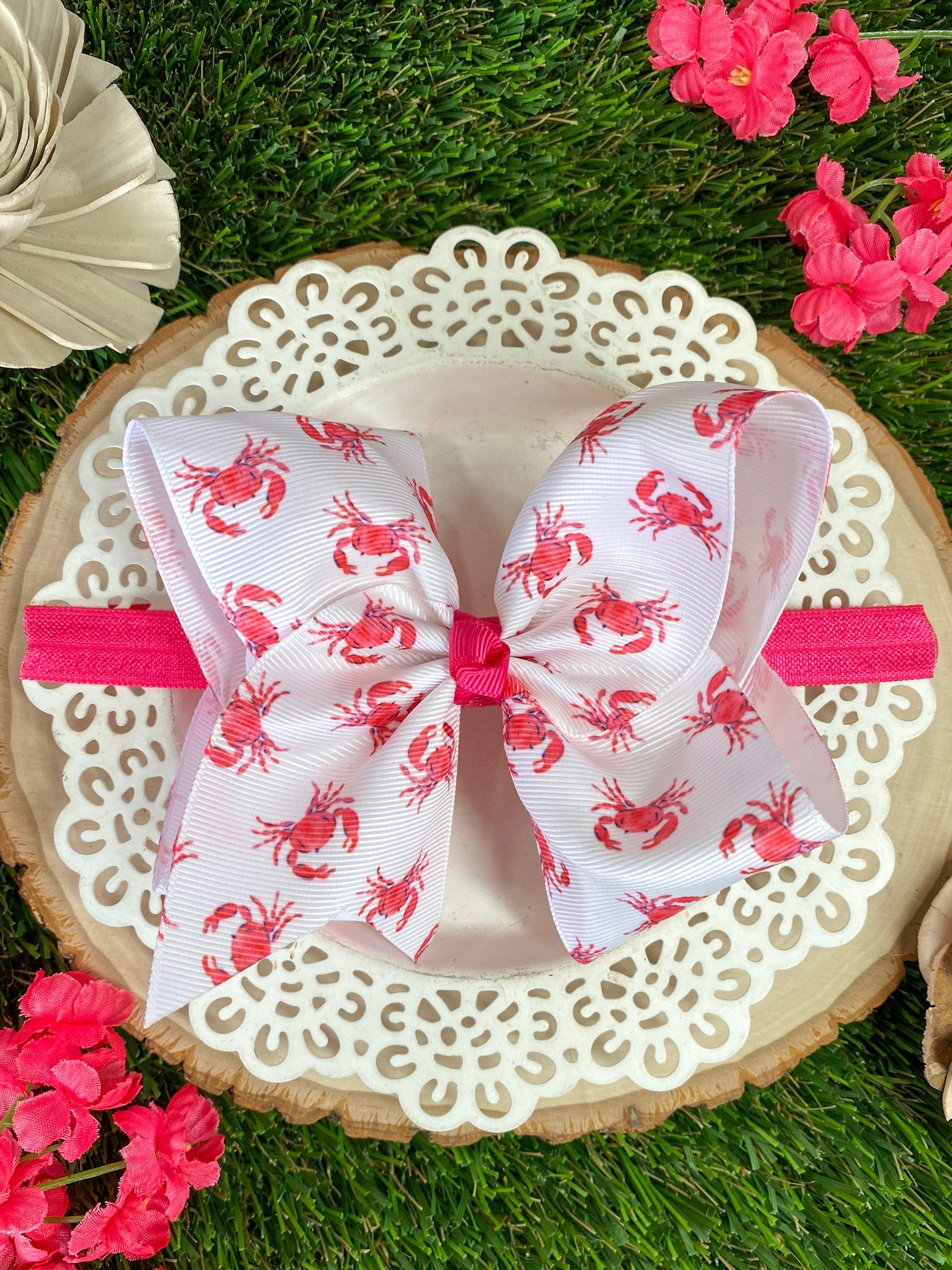 Large decorative bow with pink crab pattern on a headband, placed on a decorative stand with flowers around.