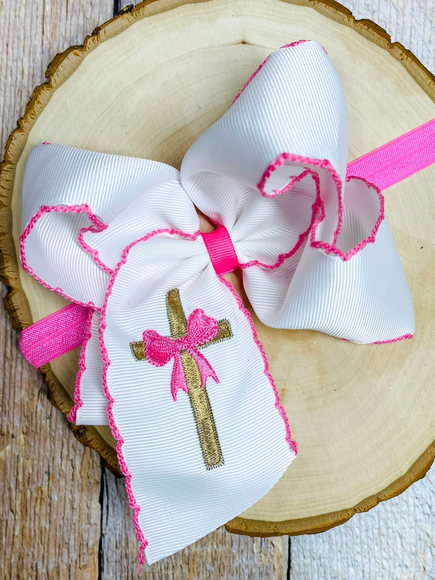 White bow with pink accents and a cross design on a wooden surface