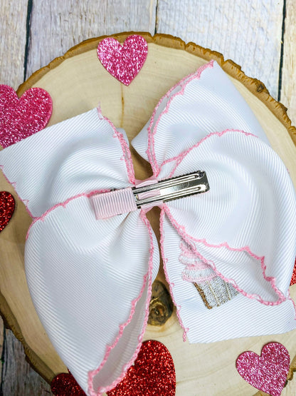 White hair bow with pink accents on a wooden surface with heart decorations