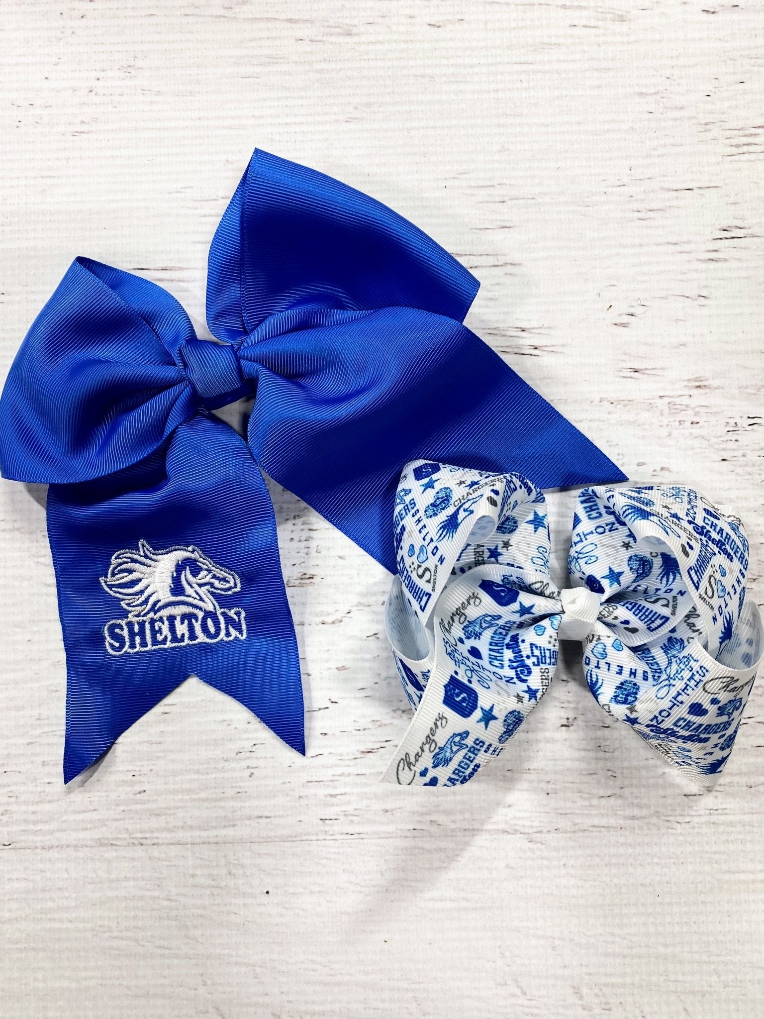 Two hair bows, one blue with a logo and the other patterned, on a light wooden surface.