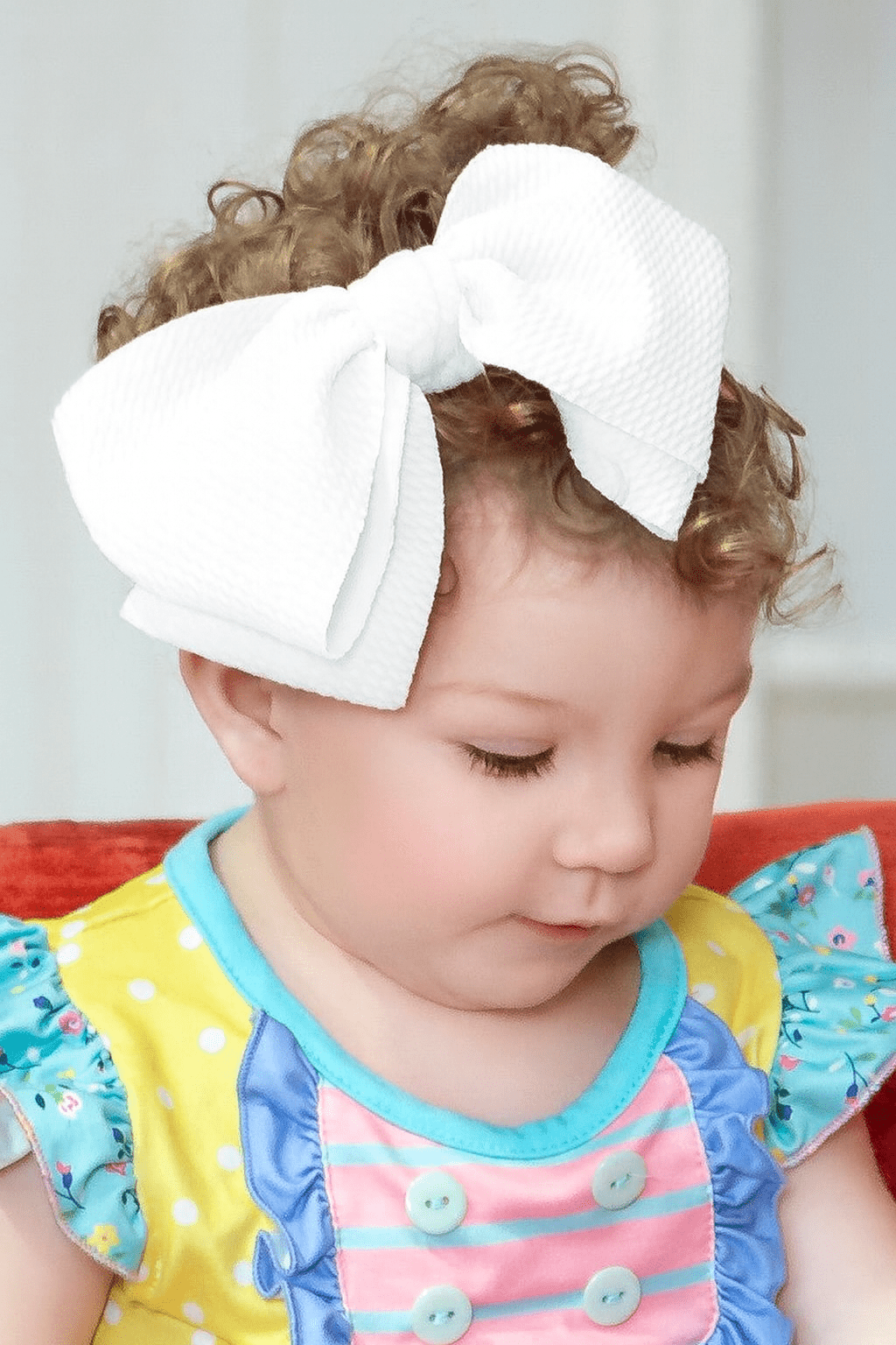 Child wearing a large white bow headband with a colorful outfit.
