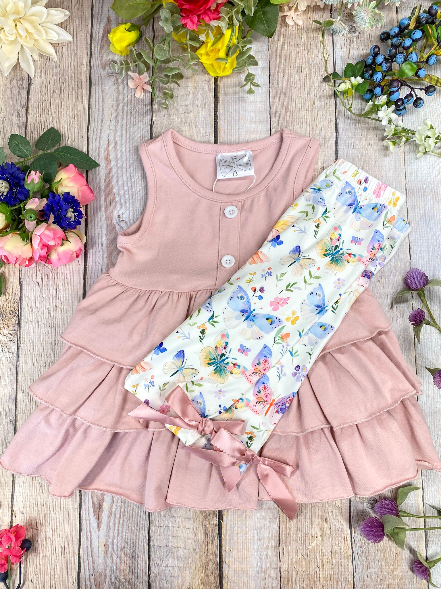 Pink tiered dress and butterfly pattern pants on a wooden background