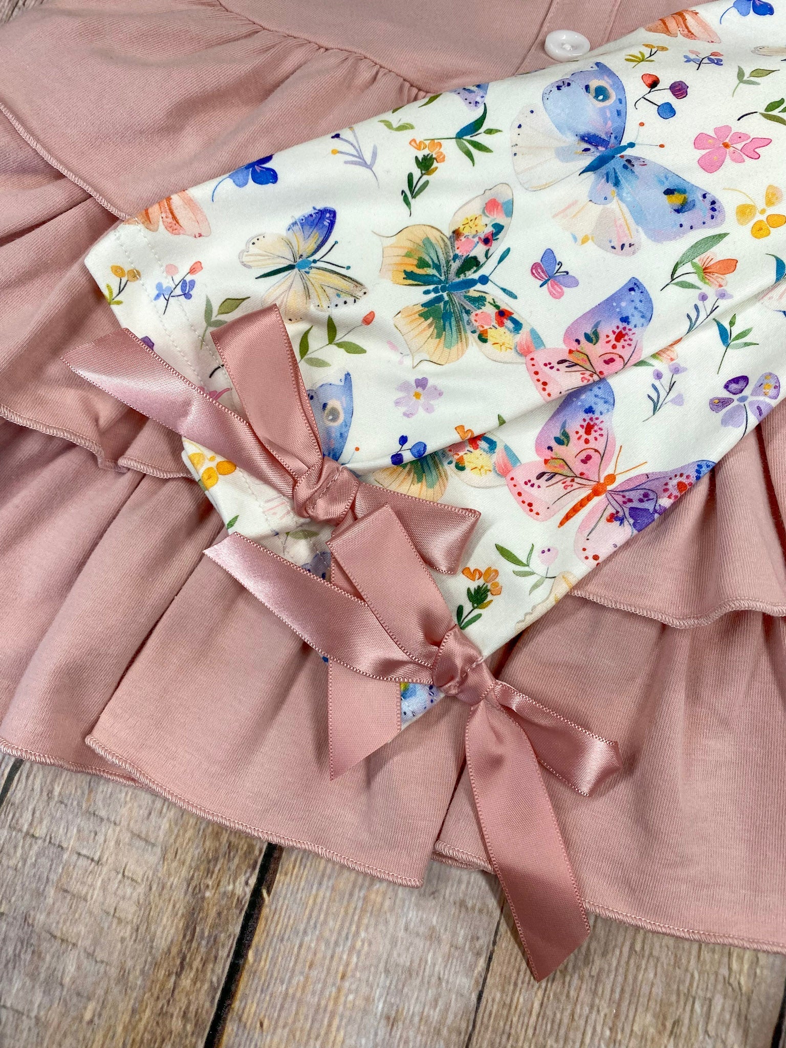 Pink tiered dress and butterfly pattern pants on a wooden background