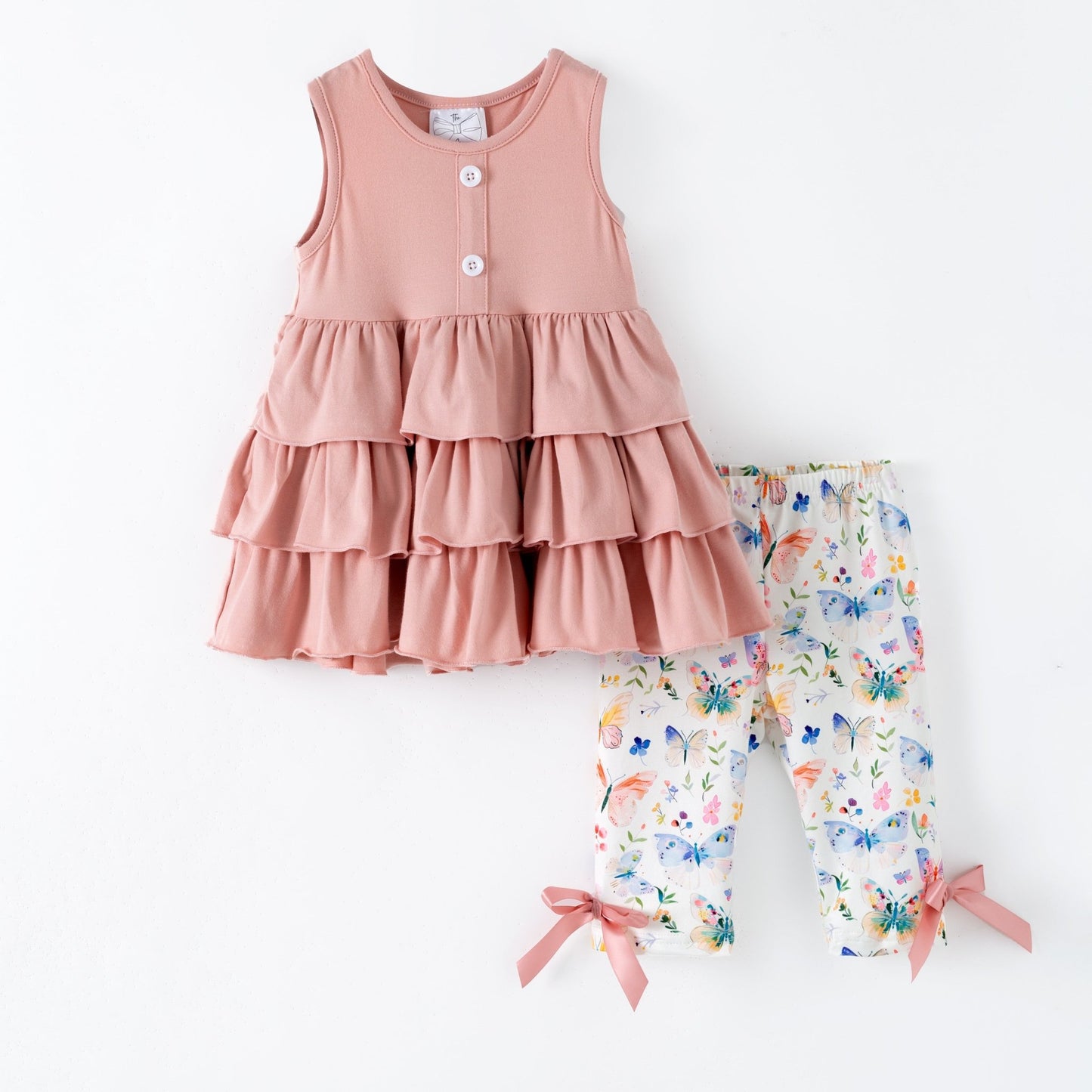 Pink tiered dress and butterfly pattern pants on a white background